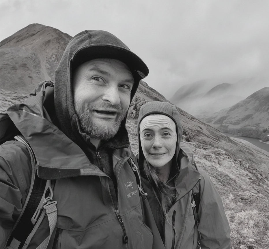 Two people in hiking gear standing in a mountainous landscape with a lake.